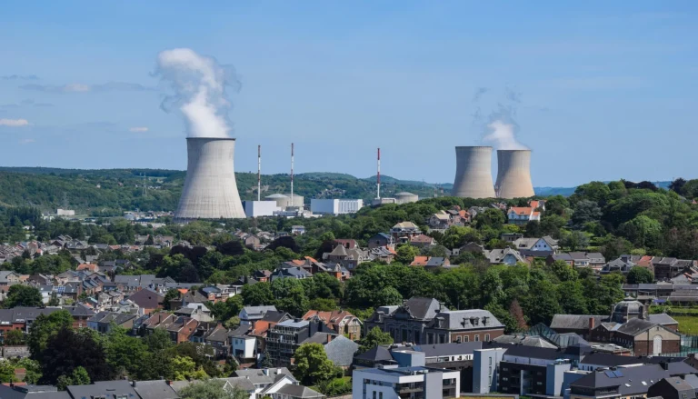 Vista panorámica de una planta nuclear con torres de enfriamiento emitiendo vapor, ubicada junto a una ciudad con casas y áreas verdes