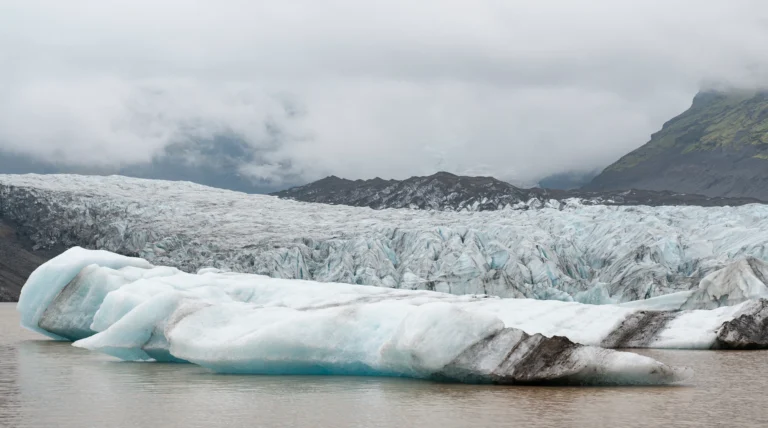 Bloques de hielo fragmentados frente a un glaciar en retroceso bajo un cielo nublado